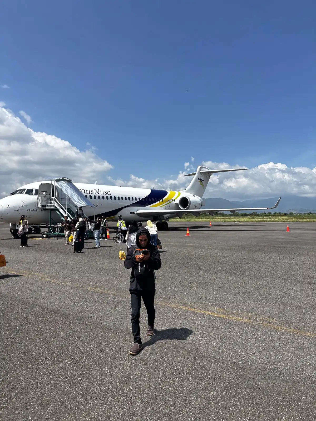 Passenger walking across the tarmac at Bima airport with a TransNusa regional jet in the background