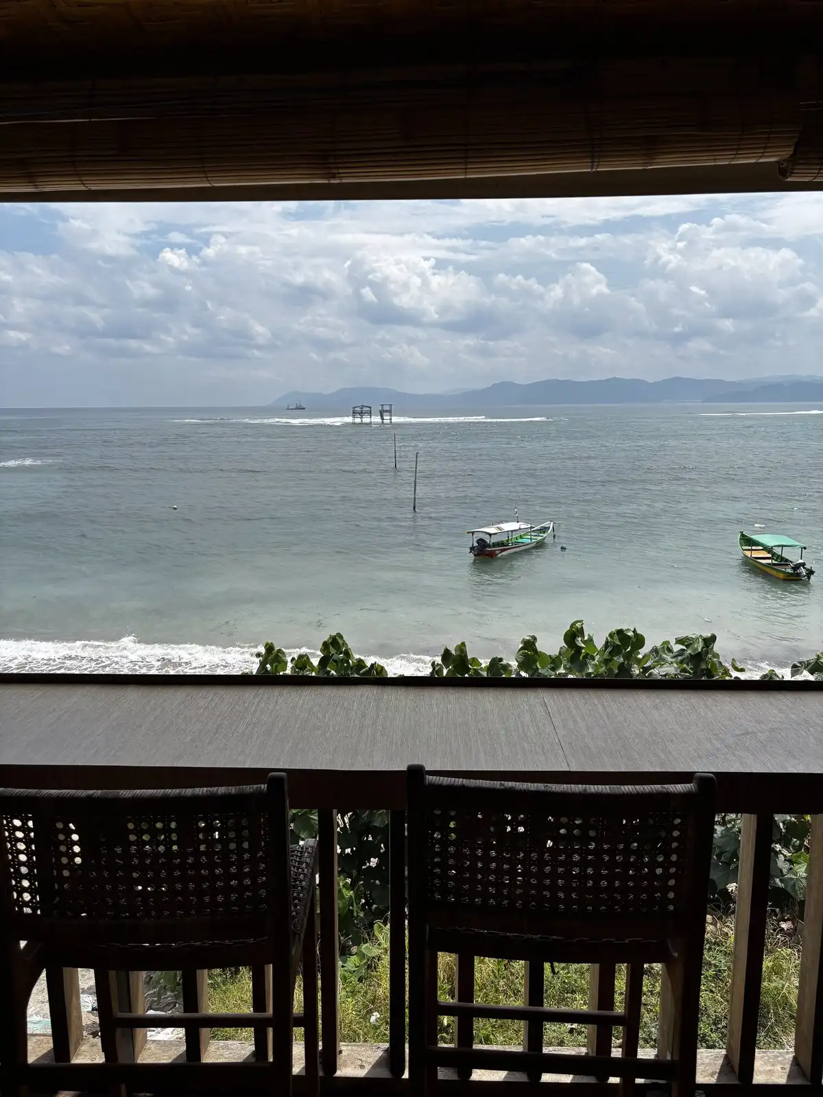 View from the cafe bar overlooking the ocean with boats on the water and waves breaking on the reef at Lakey Peak, wooden chairs in the foreground