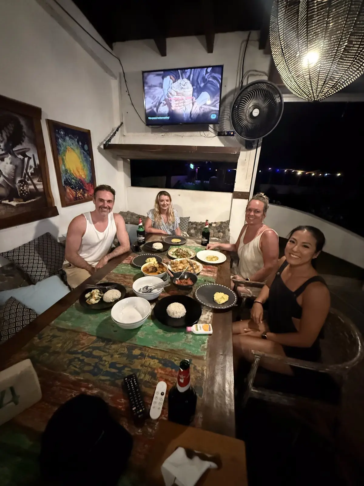 Group of four people sharing dinner at a local restaurant in Lakey Peak, plates of Indonesian food spread across a rustic wooden table