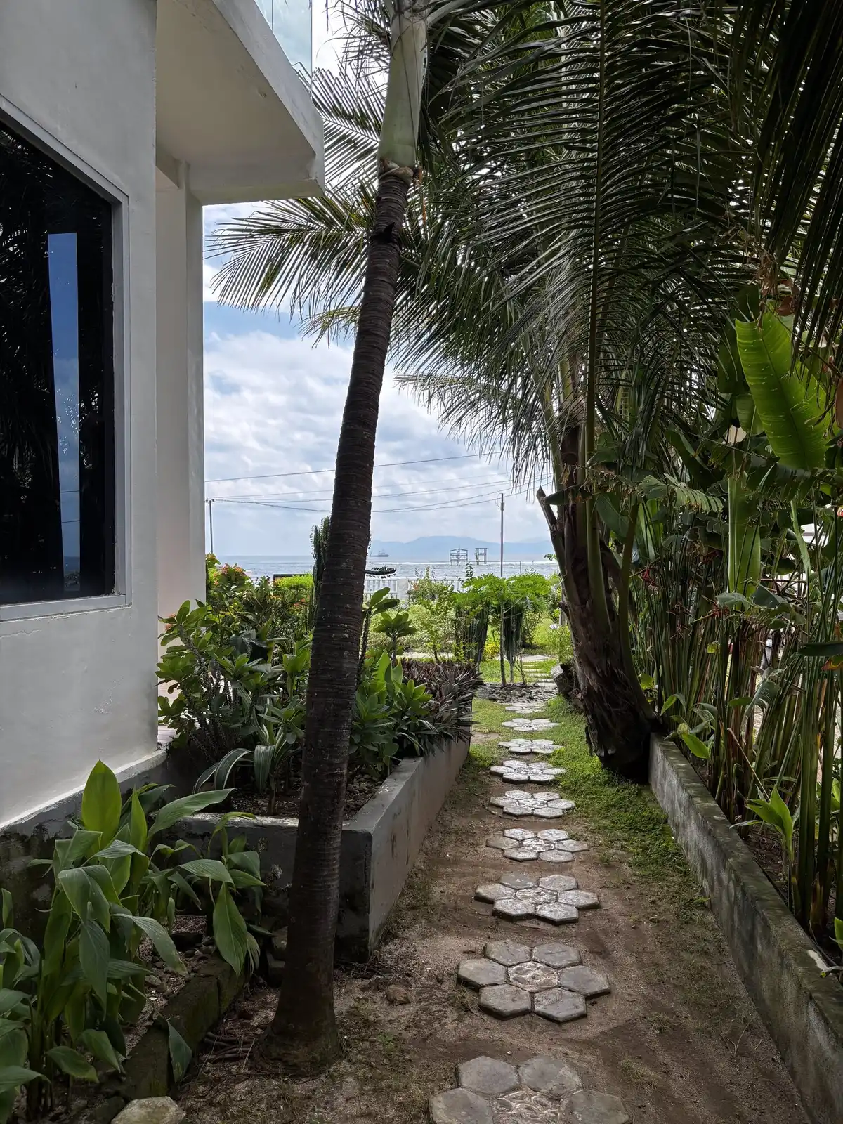 Tropical garden pathway with hexagonal stepping stones winding between palm trees and flowering plants toward the ocean at the accommodation