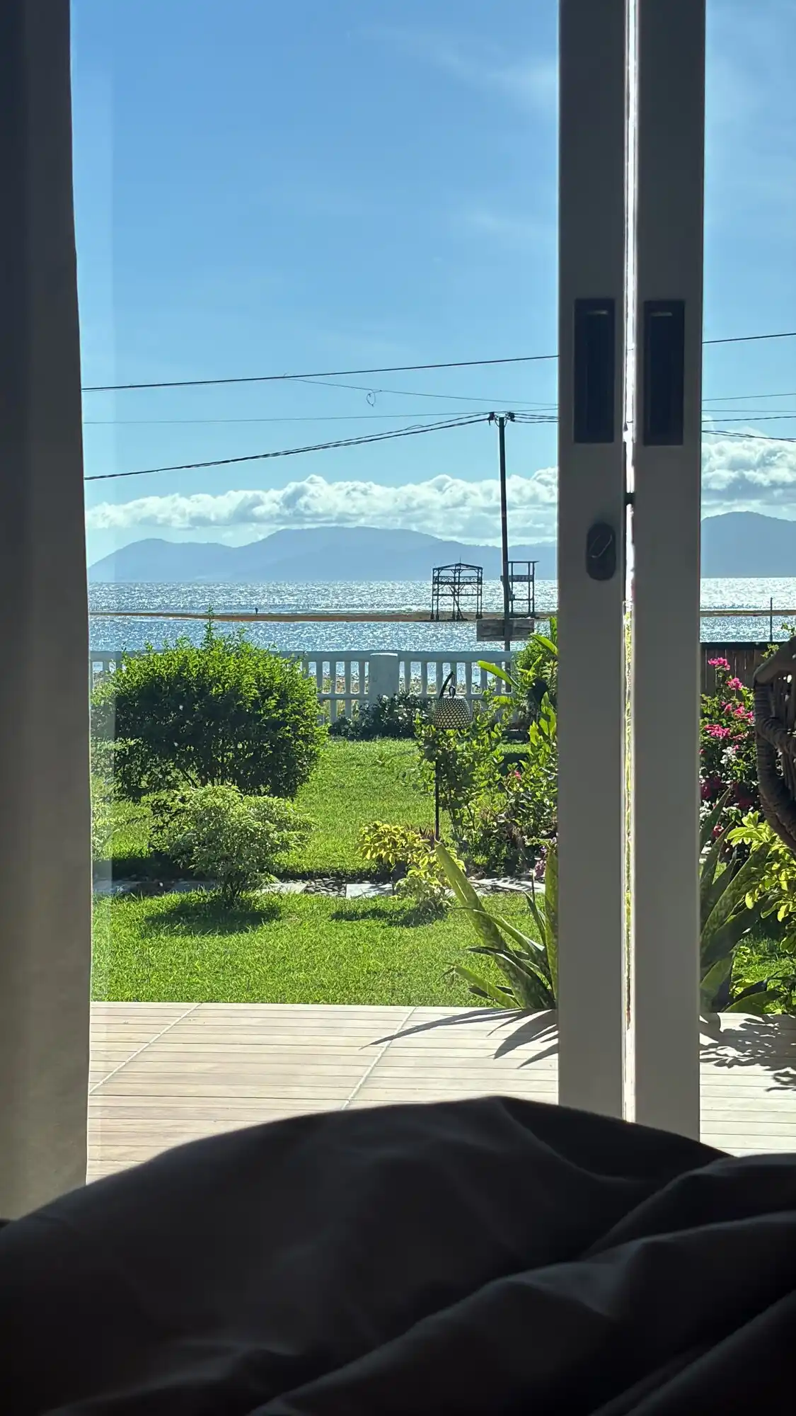 Morning ocean view from the room at Peak Surf House, green lawn and tropical garden leading to the beachfront with mountains across the water