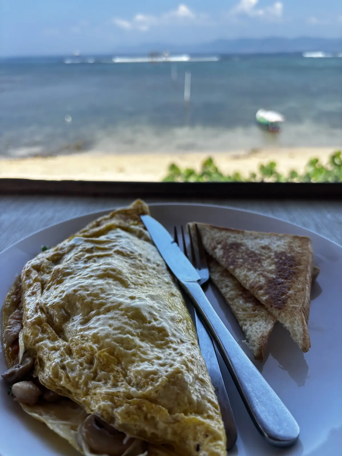 Omelette and toast served at the beachfront restaurant with the sandy beach and ocean stretching out behind