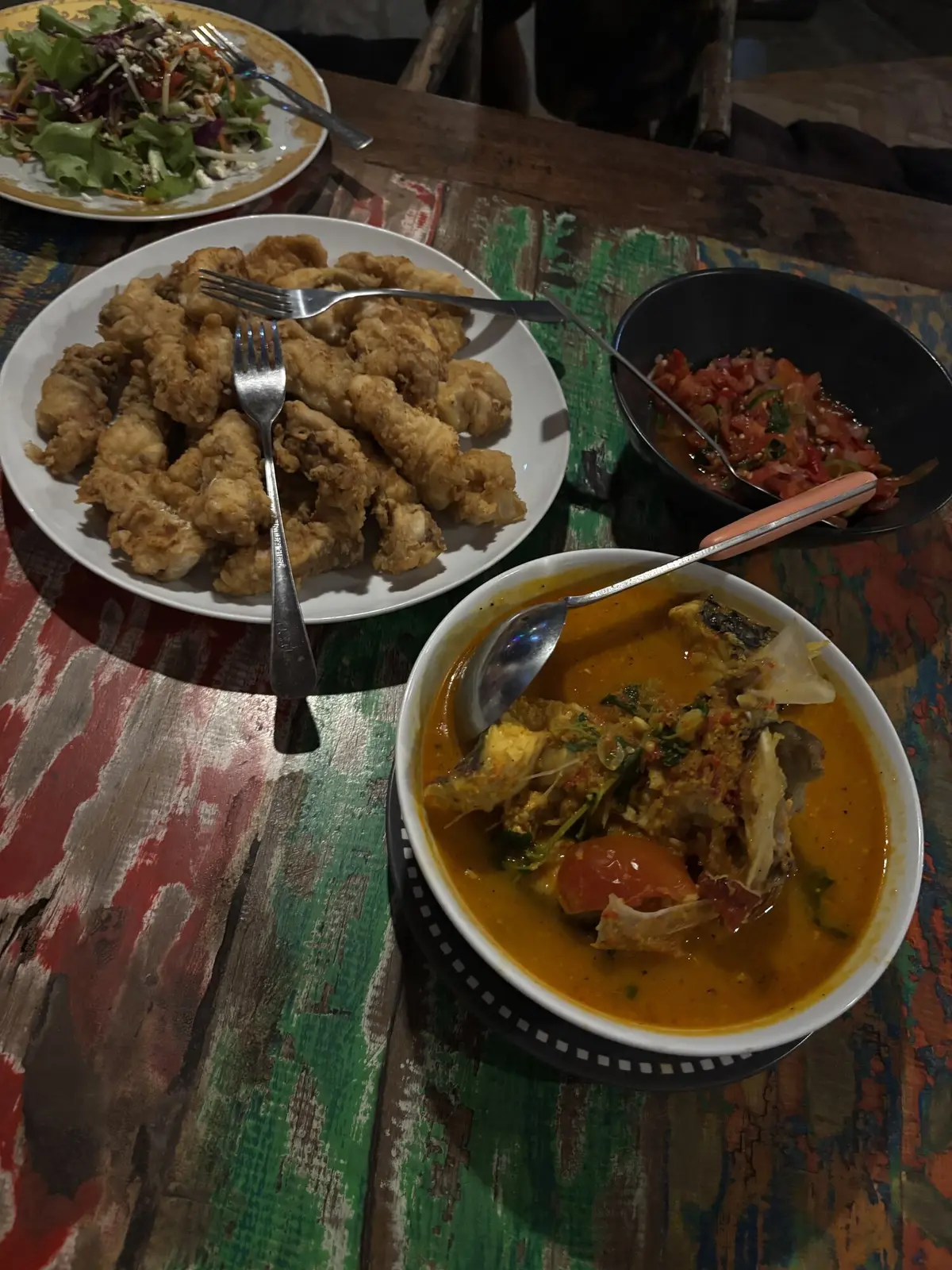 Spread of fresh-caught fish curry, fried calamari, salad and sambal on a colourful painted wooden table at Three Waves Cafe after a spearfishing trip