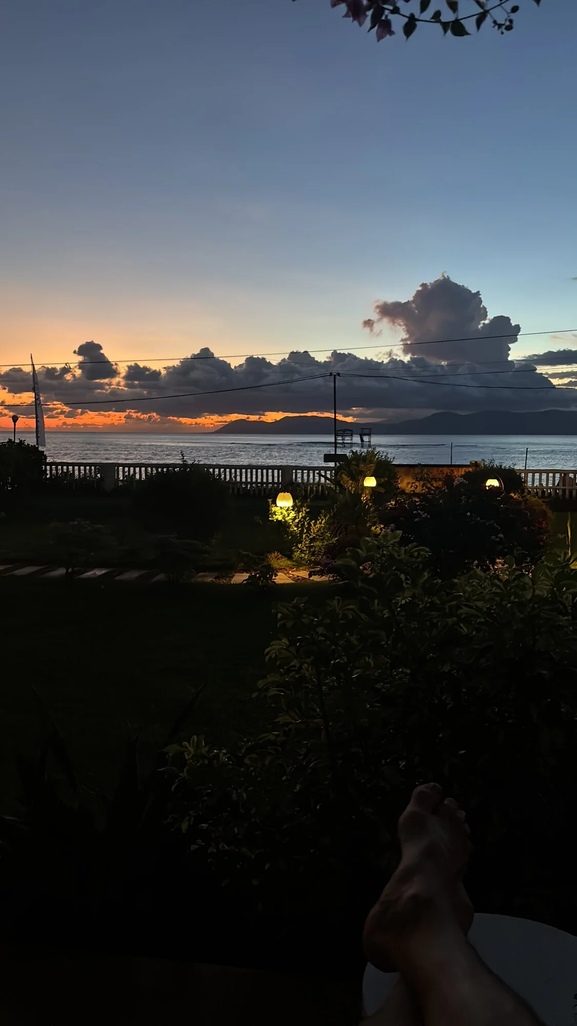 Sunset over the ocean from the Peak Surf House patio, garden lights glowing below orange and purple clouds