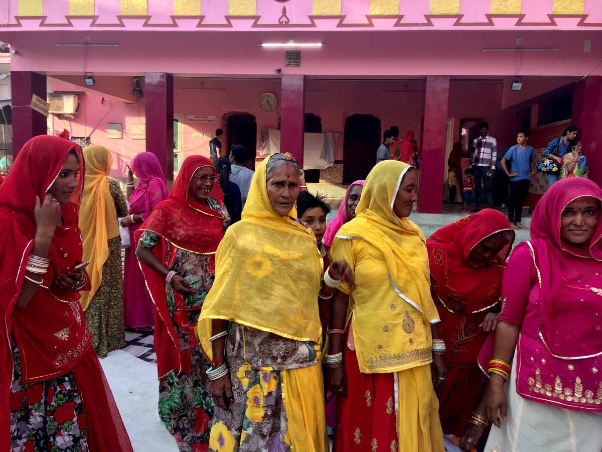 Women in vibrant pink red and yellow saris gathered at a Rajasthan temple