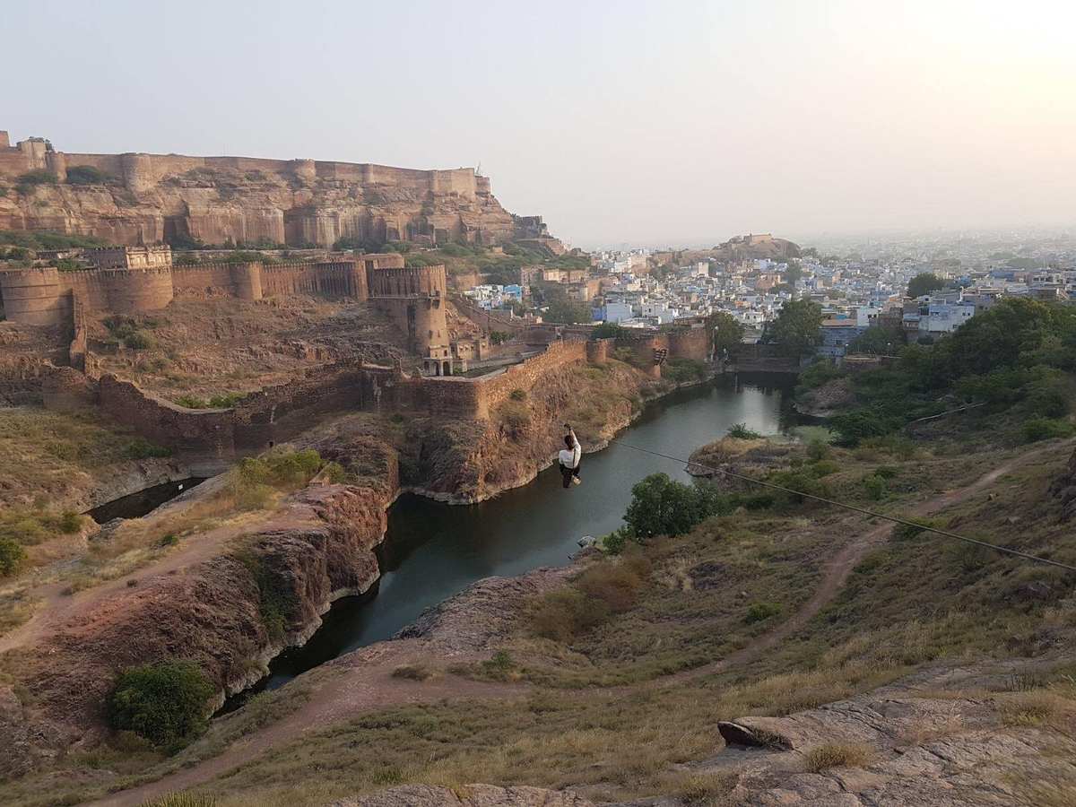 Wide view of a zipline crossing the moat below Mehrangarh Fort with Jodhpur blue city beyond