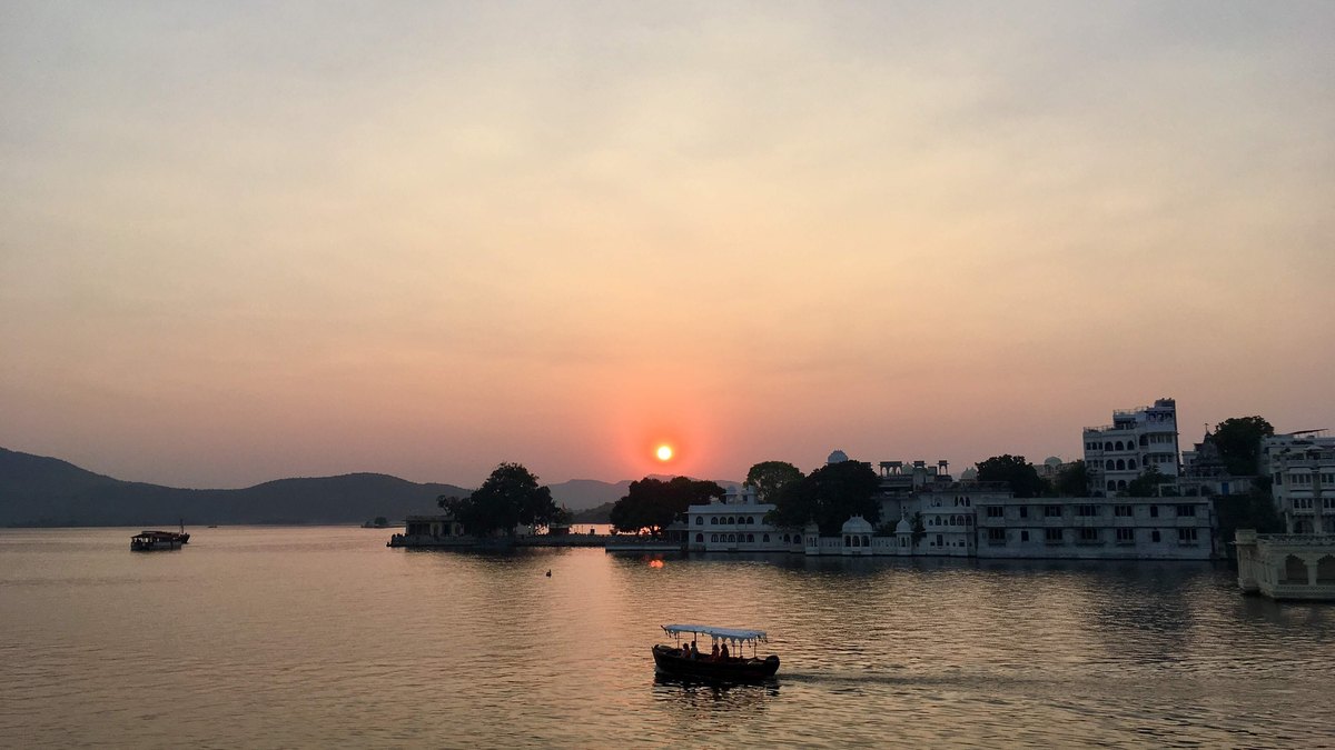 Sunset over Lake Pichola with a single boat and the white Lake Palace in Udaipur