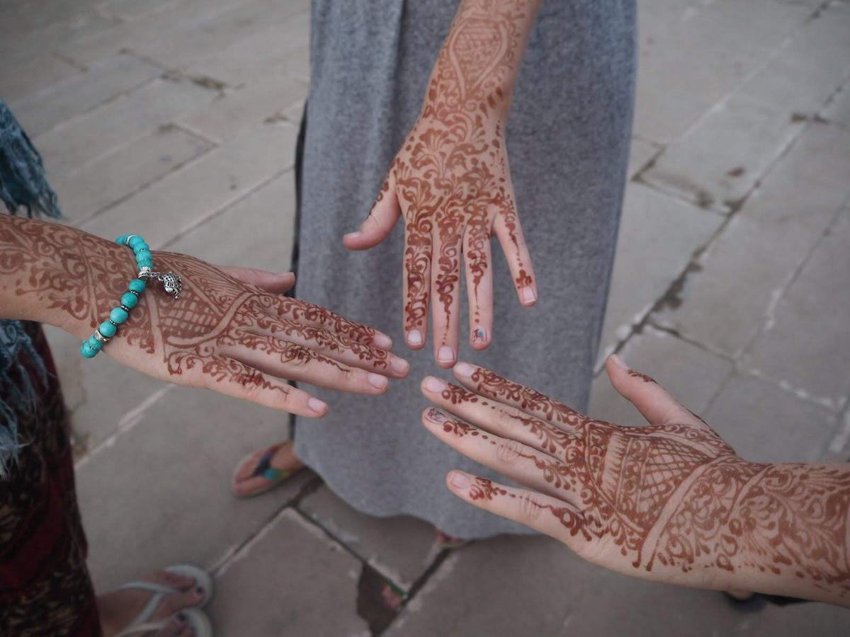 Three hands showing intricate mehndi henna designs with a turquoise bead bracelet