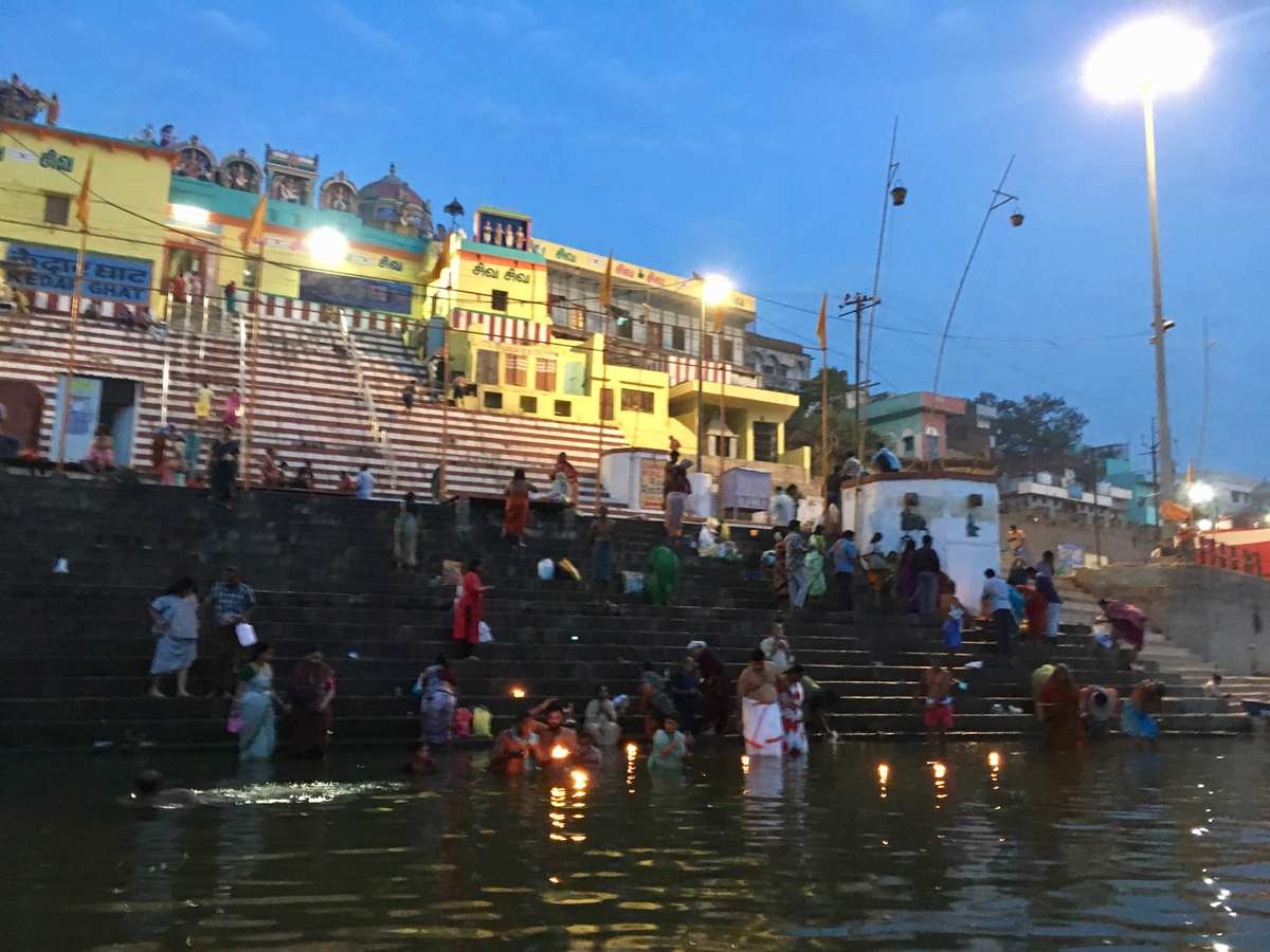 Evening bathing and floating diyas at Kedar Ghat with a colorful striped temple behind
