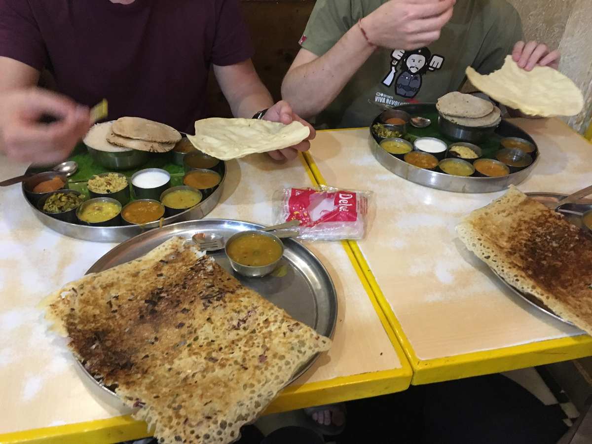 Traditional South Indian thali with steel bowls of curry alongside crispy dosa at a local restaurant