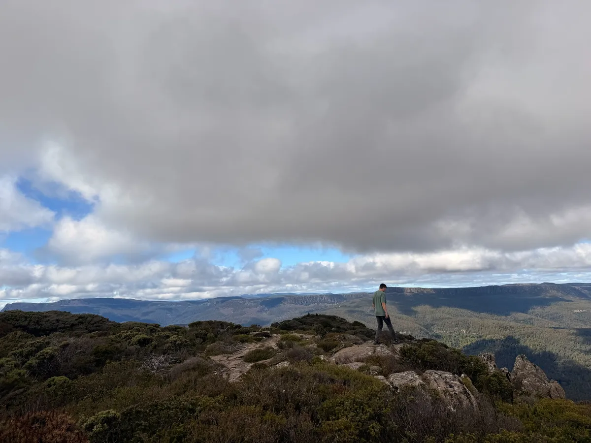 Hiker standing on exposed summit rocks of Quamby Bluff looking out over northern Tasmania