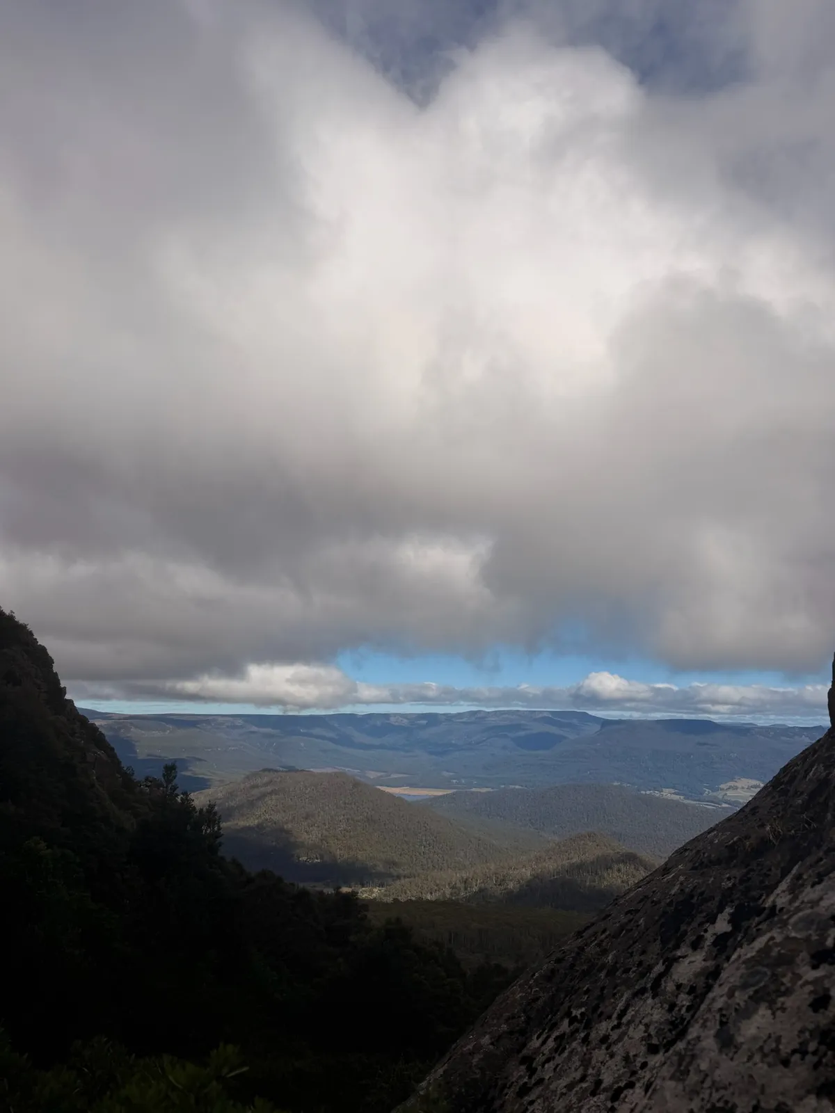 Moody summit view through a gap in the dolerite rocks looking out over distant mountain ranges and valleys under heavy cloud
