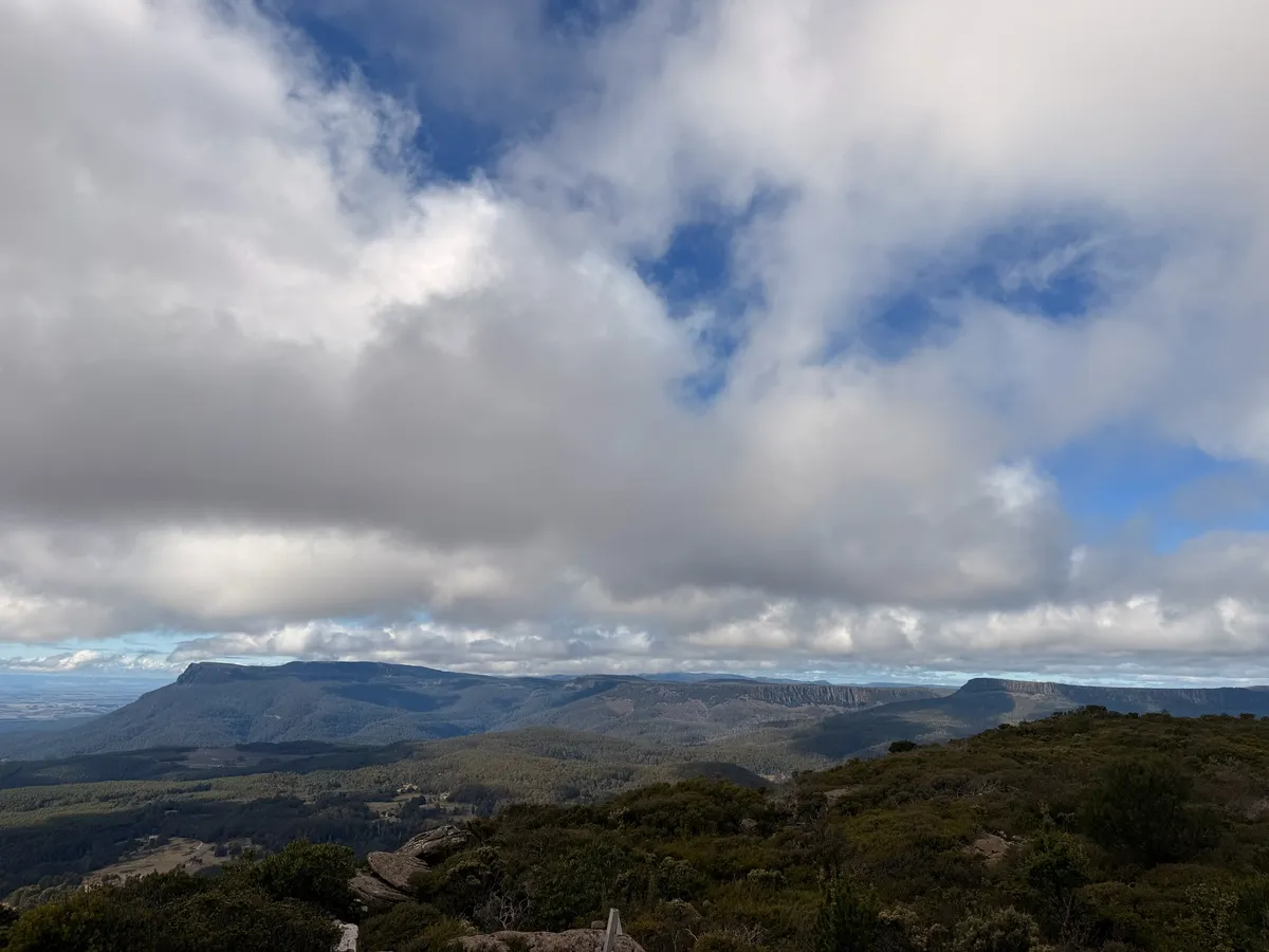 Wide panoramic view from Quamby Bluff summit showing flat-topped mountains, green farmland, and rolling hills of northern Tasmania